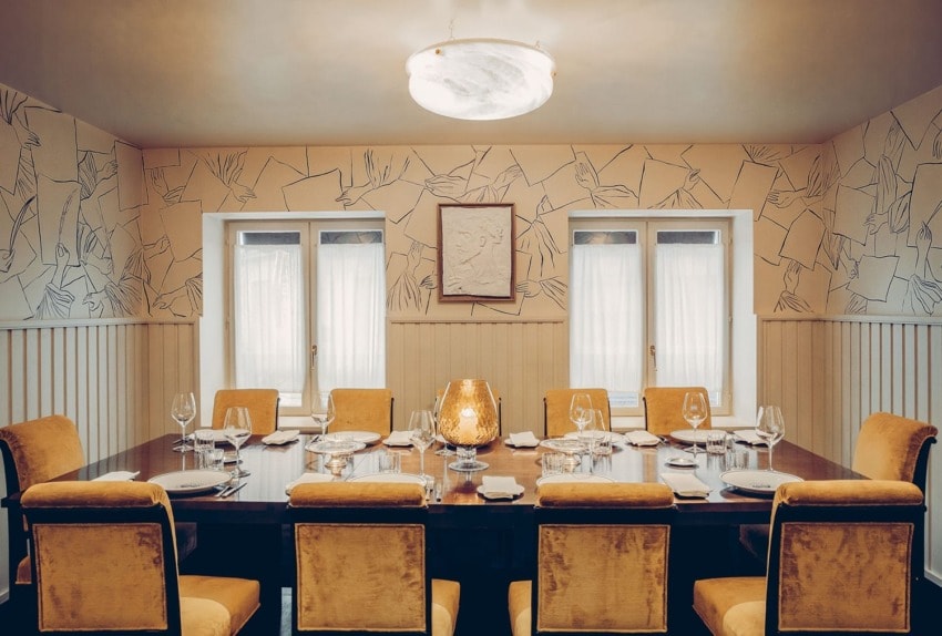 Elegant dining room with a large table, set with plates and glasses, surrounded by plush chairs under a modern light fixture.