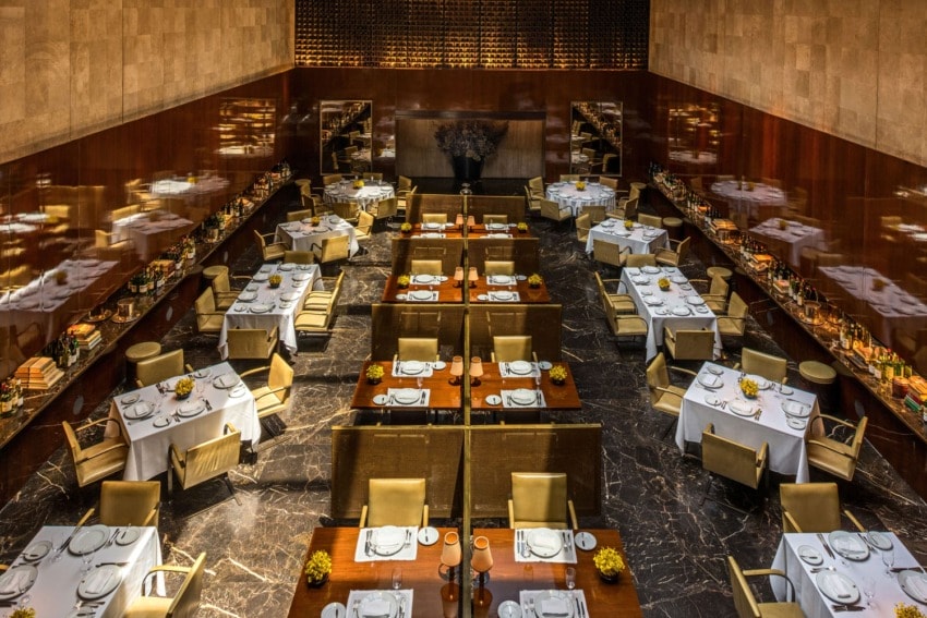 Elegant restaurant interior with neatly set dining tables, golden chairs, and warm lighting.