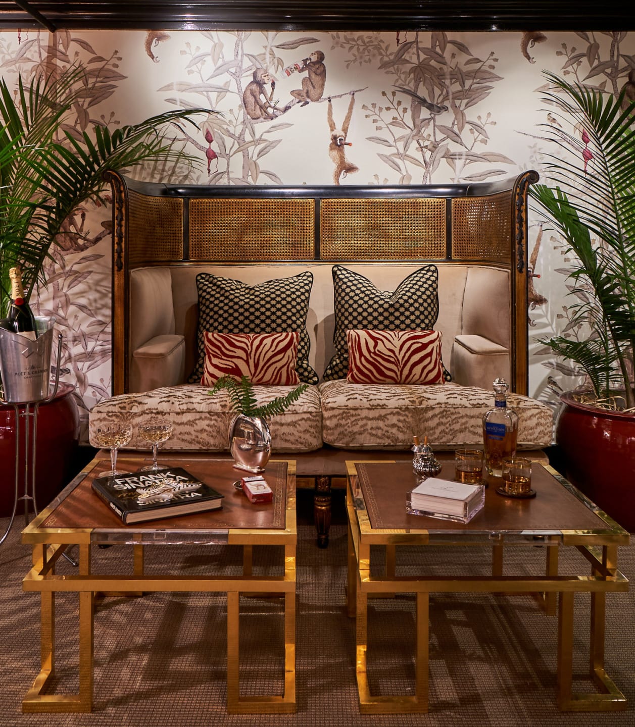 Elegant seating area with two zebra-patterned pillows, golden coffee tables, ornate wallpaper, and plants in an upscale setting.
