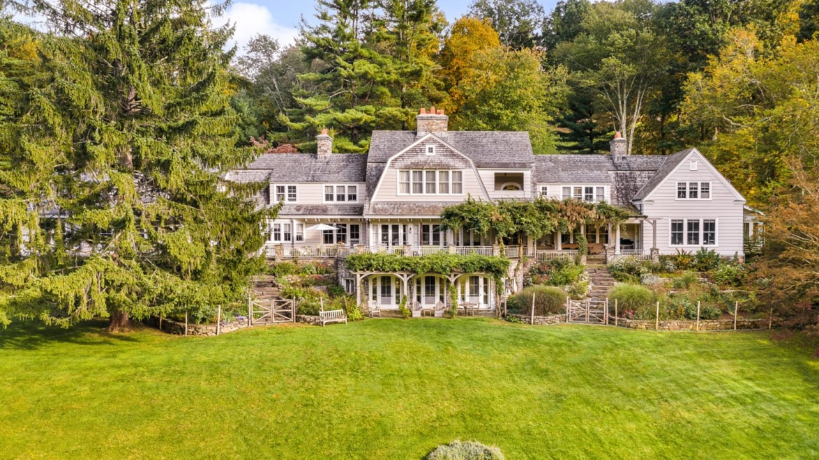 Large picturesque country house with lush greenery and tall trees in the background.