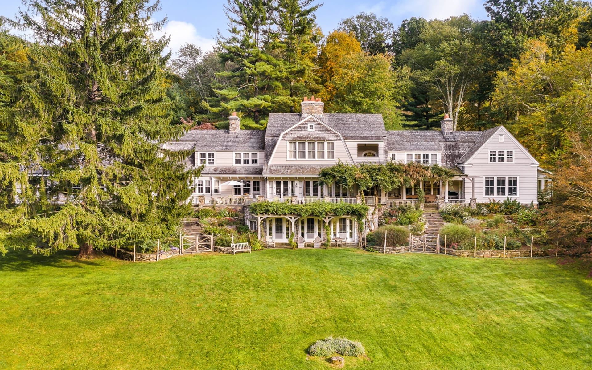 Large picturesque country house with lush greenery and tall trees in the background.