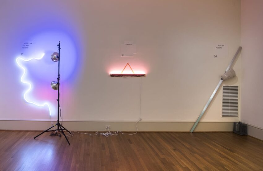 Art installation with neon lights on a gallery wall, featuring a face outline, light bulbs, and various light fixtures.