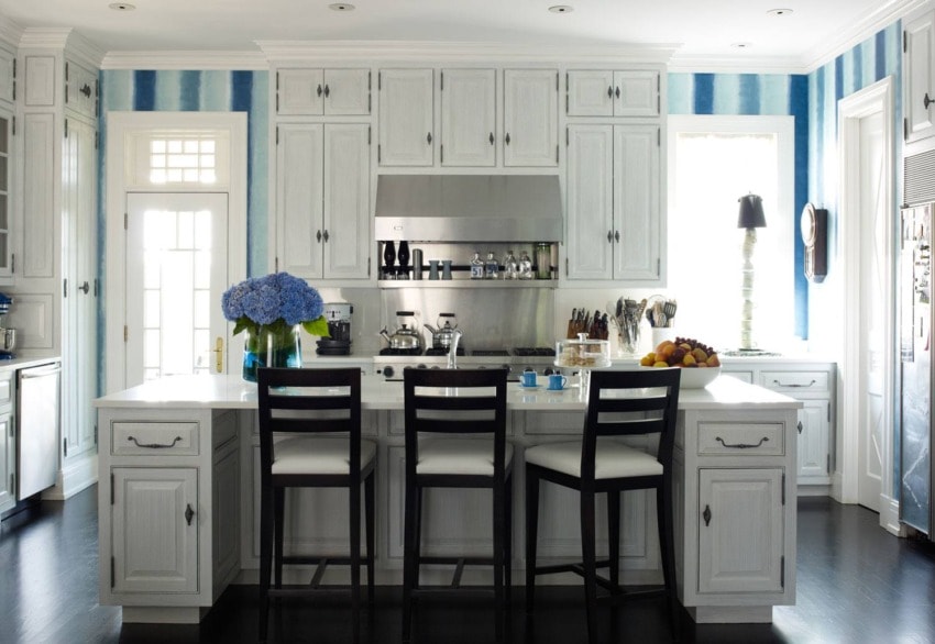 Modern kitchen with white cabinets, island, striped blue wallpaper, and a vase of blue flowers on the countertop.