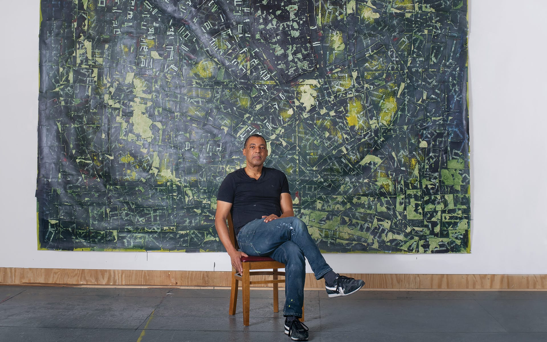 Artist seated in front of a large abstract painting in a studio setting.