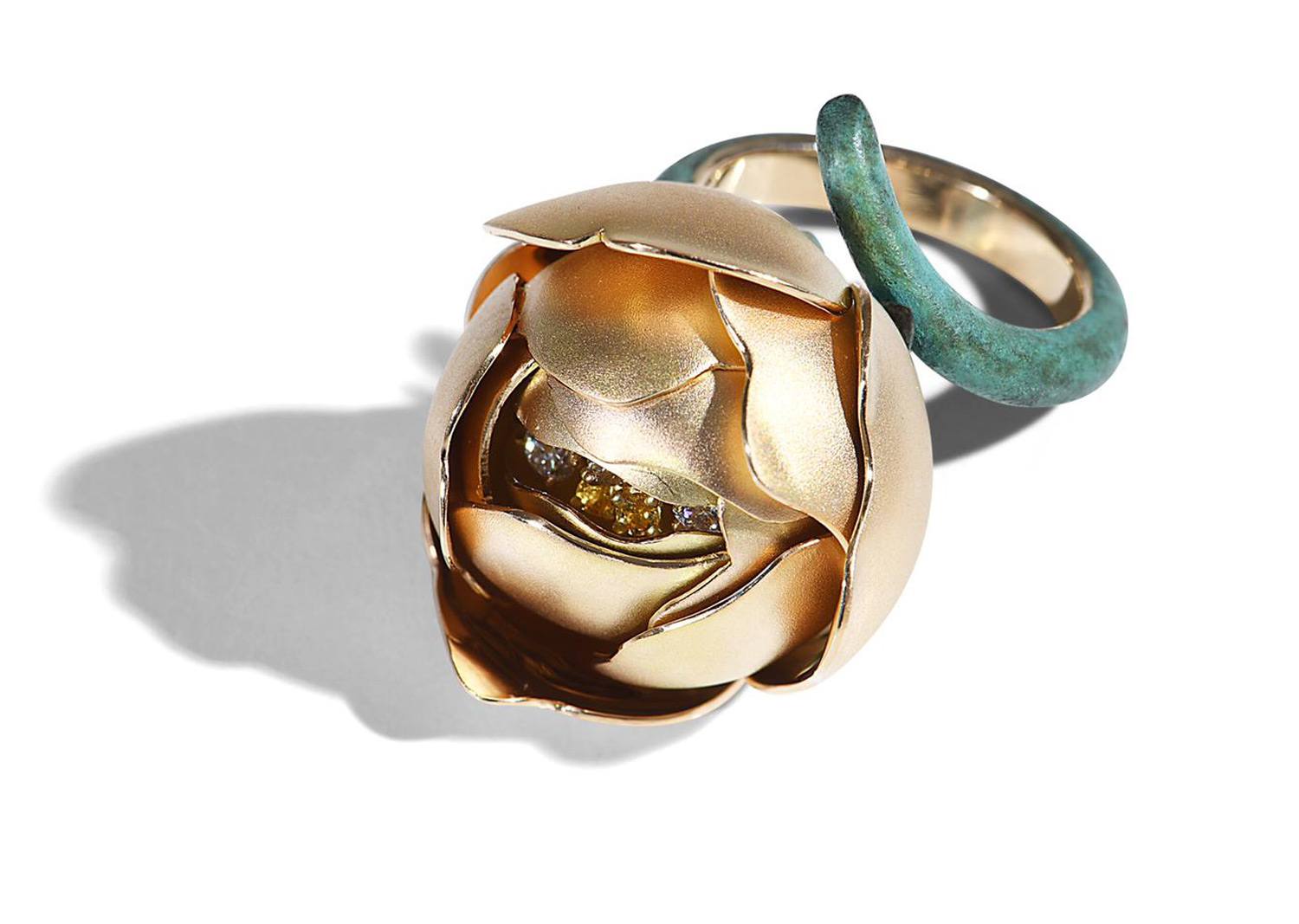 Gold lotus-shaped ring with a diamond center and a green band, casting a shadow on a white background.