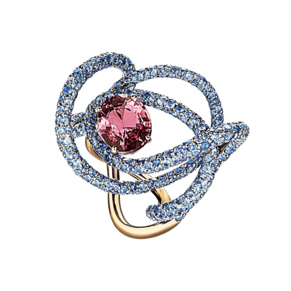 Gold ring with an intricate design featuring a central pink gemstone surrounded by blue gemstones in abstract loops.