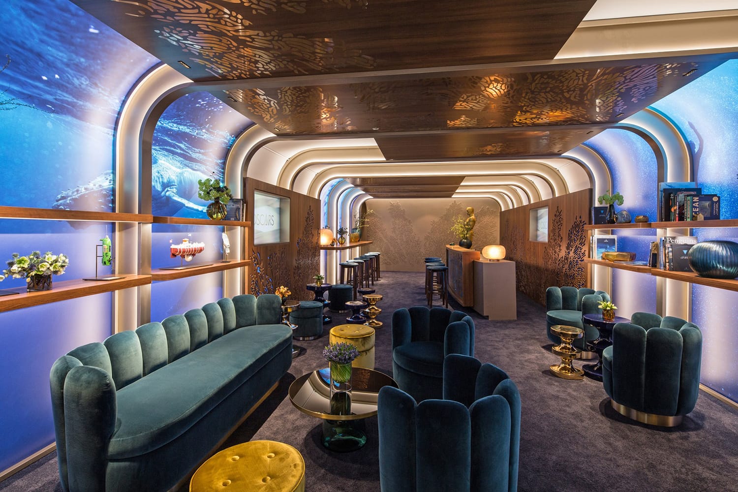 Luxurious lounge with blue velvet seating, golden accents, ambient lighting, and ocean-themed walls creating an elegant atmosphere.