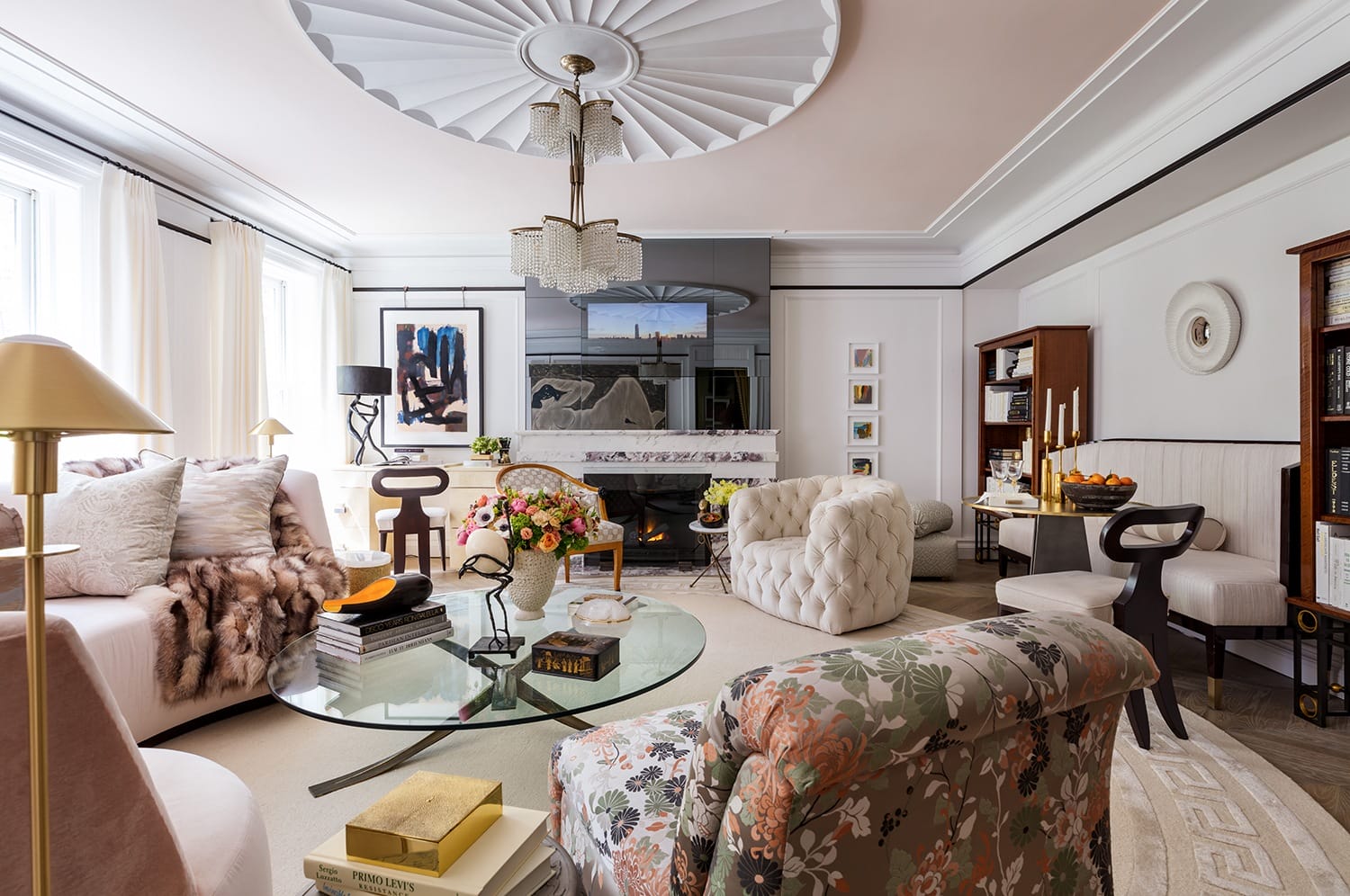 Elegant living room with plush chairs, floral accents, round glass coffee table, and large mirror above a fireplace.