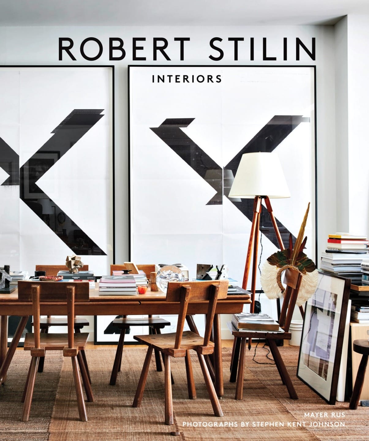 Modern dining room with wooden furniture, books, large black and white artwork, and floor lamp against a neutral backdrop.