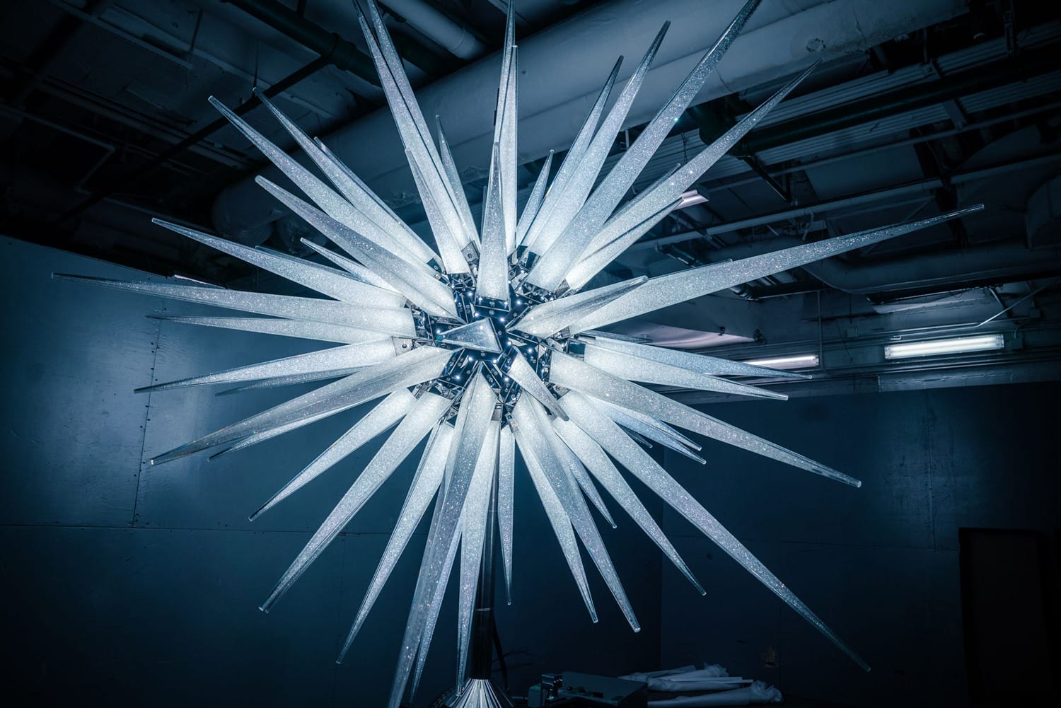 Futuristic star-shaped light fixture with glowing spikes in an industrial setting.