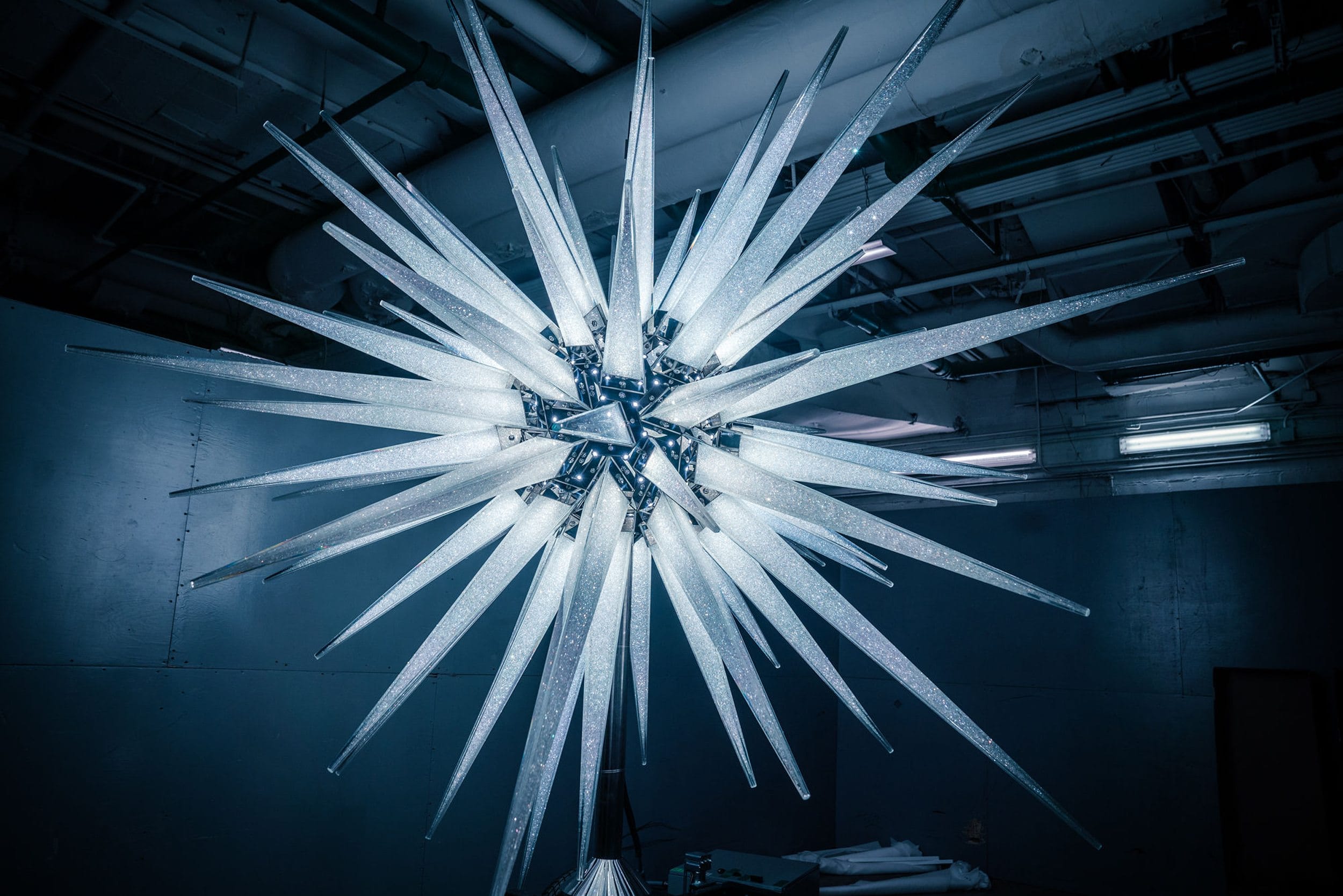 Modern starburst chandelier with glowing spikes in an industrial setting.