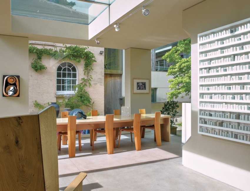 Modern dining area with wooden table and chairs, large window, skylight, and wall art in a bright, contemporary setting.