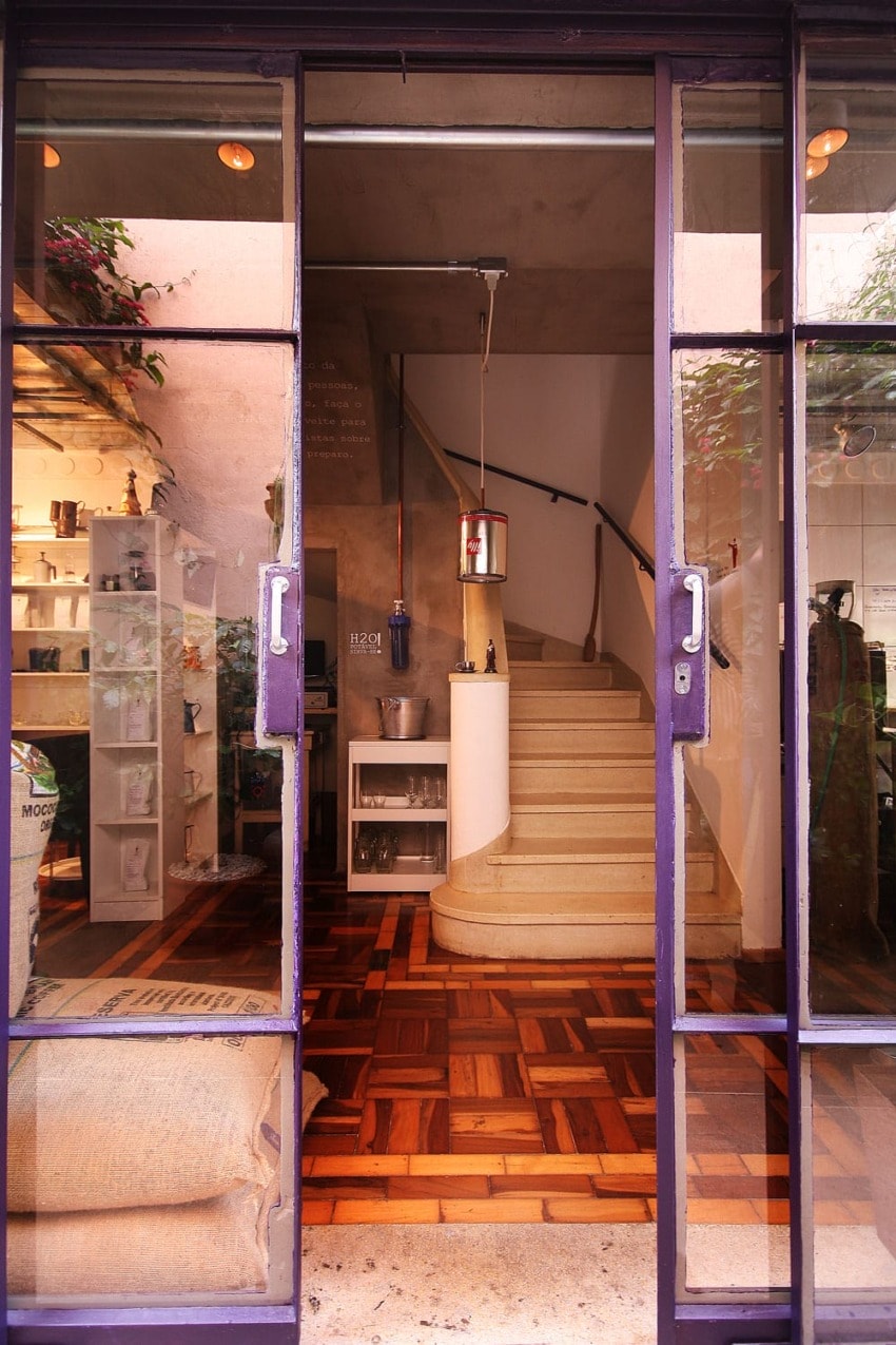 Entrance of a boutique shop with wooden flooring, staircase, and shelves displaying various products in a well-lit space.
