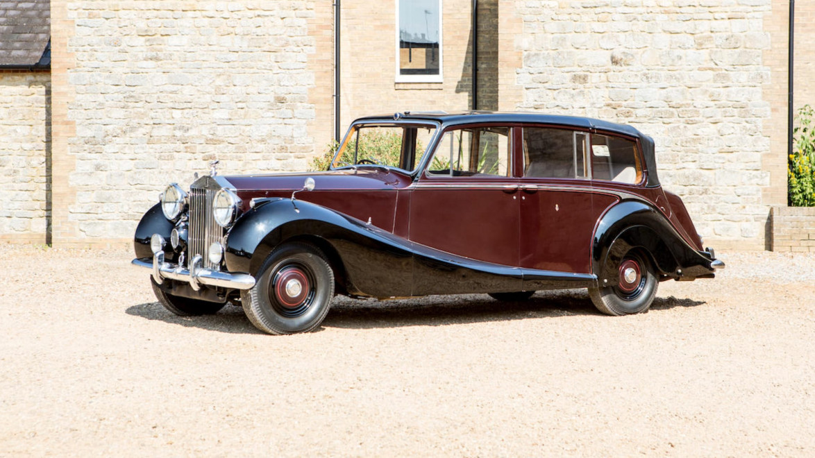 Vintage dark burgundy classic car parked on gravel with brick building in the background