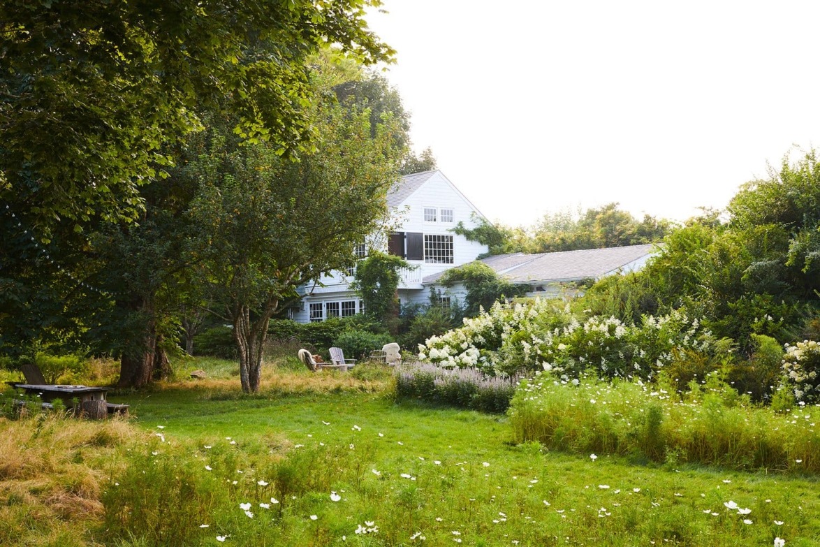 White house surrounded by lush greenery and wildflowers with a garden and outdoor seating area in the foreground