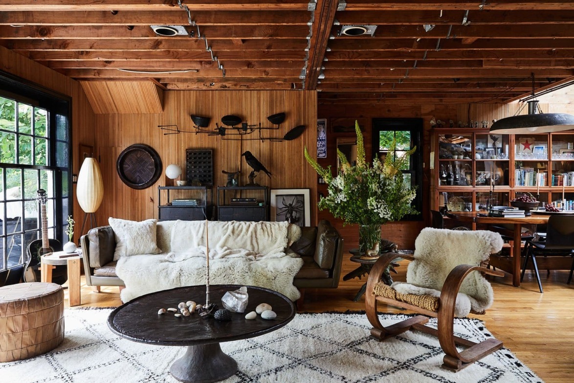 Cozy living room with wooden ceiling, furniture, large window, eclectic decor, and a textured rug on wooden flooring.