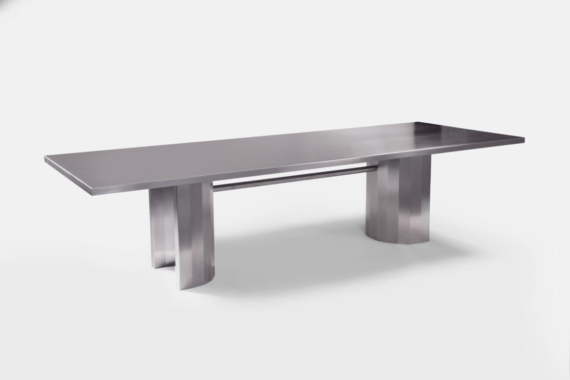 Modern stainless steel dining table with a sleek design and sturdy double pedestal base against a white background.