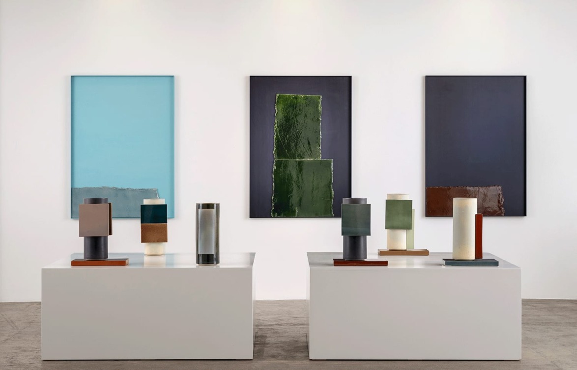 Art gallery display with modern sculptures on pedestals and three abstract paintings in the background.