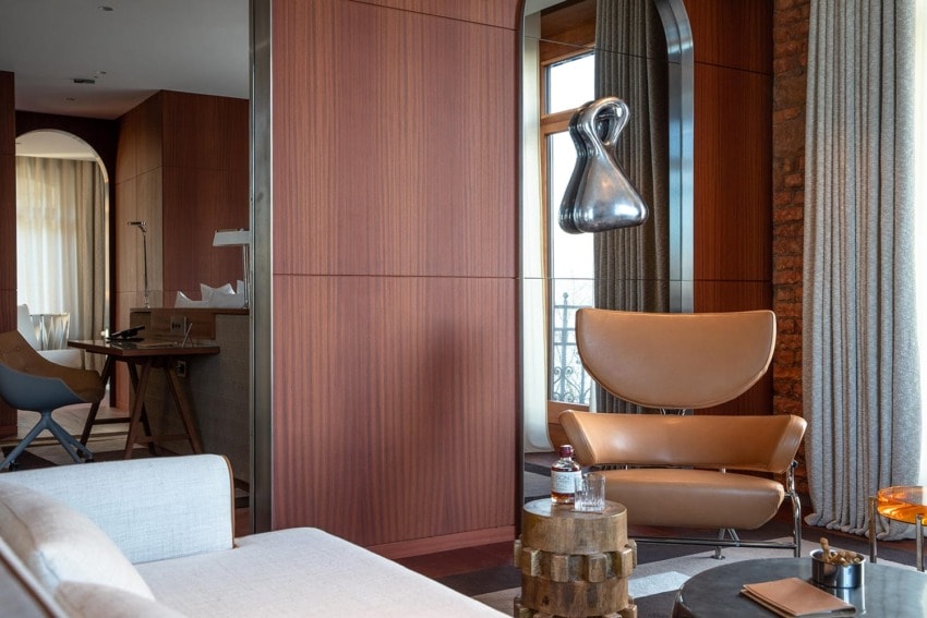 Modern lounge area with leather chair, unique wooden side table, hanging light fixture, and large window with white curtains