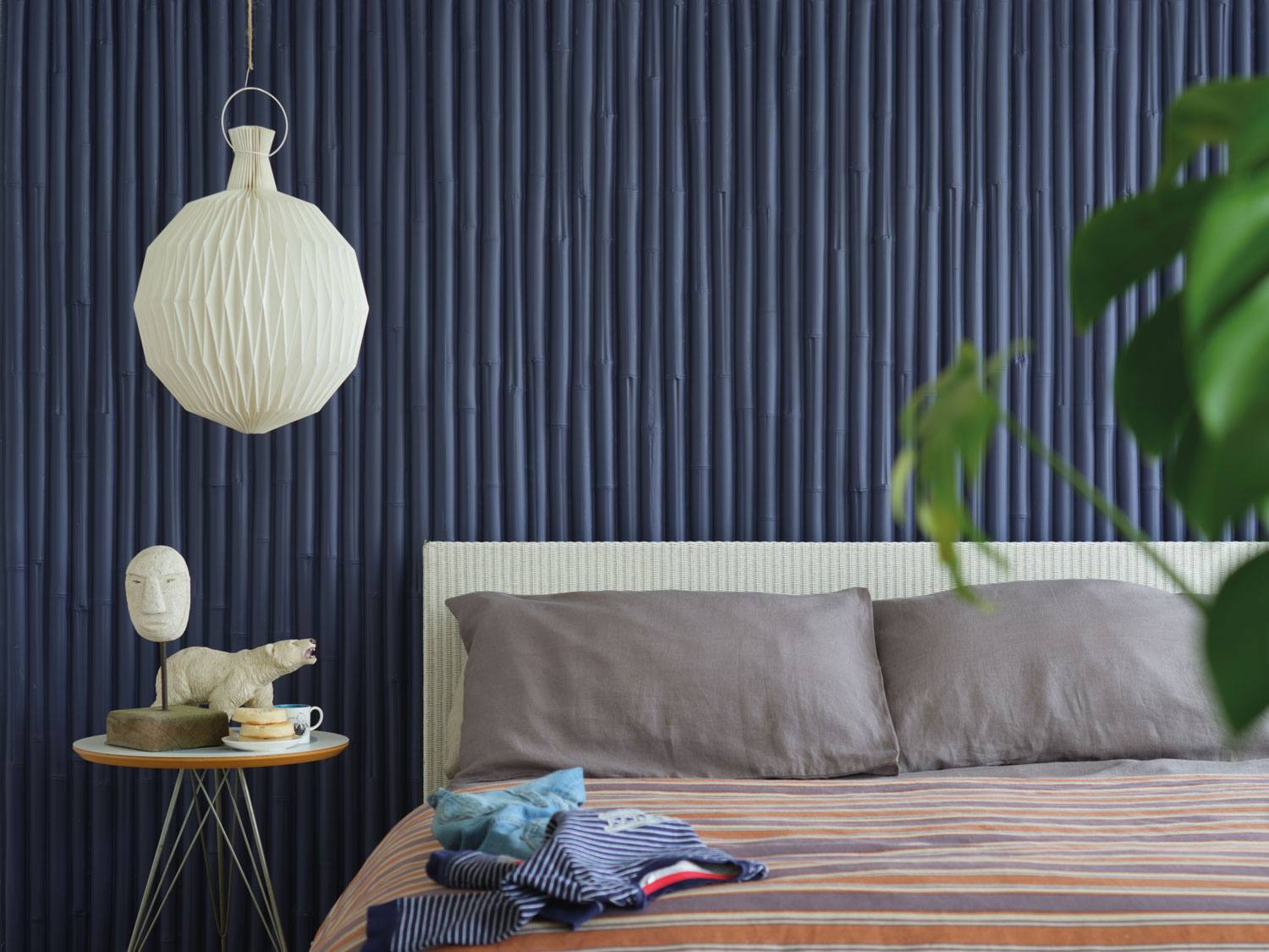 Modern bedroom with a striped bedspread, a round side table, a unique pendant lamp, and a textured dark blue wall.