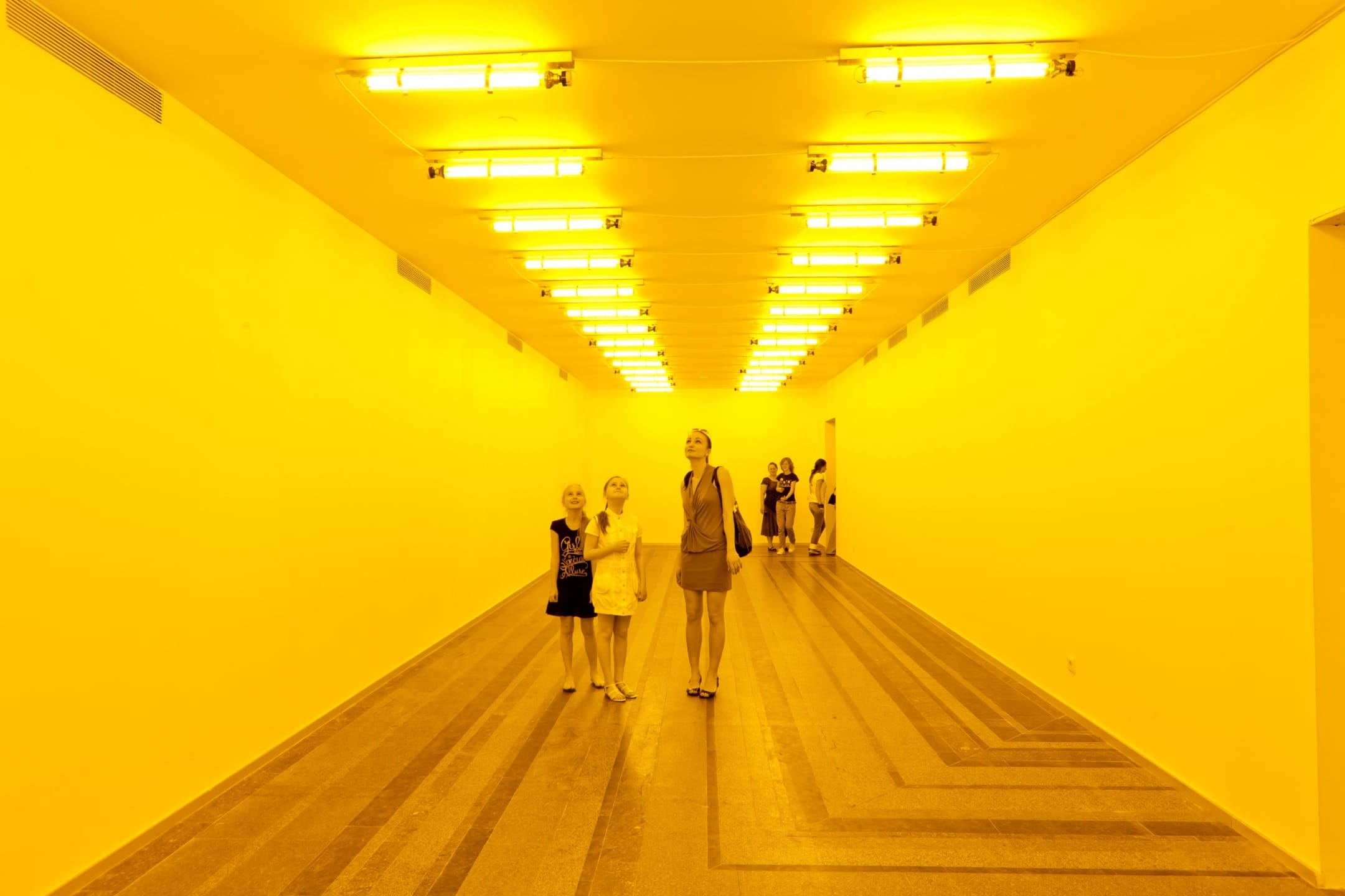 People walking through a hallway lit with yellow lights, creating a bright and colorful atmosphere.