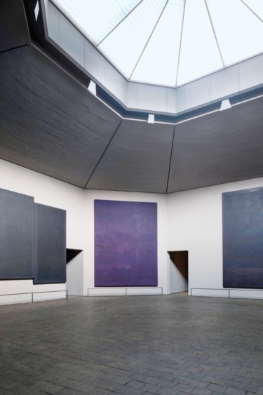 Interior view of a modern art gallery with large abstract paintings and a skylight ceiling.