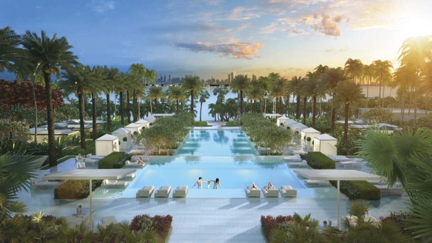 Luxurious resort pool area with palm trees, cabanas, and people relaxing, overlooking a scenic sunset view of the water.