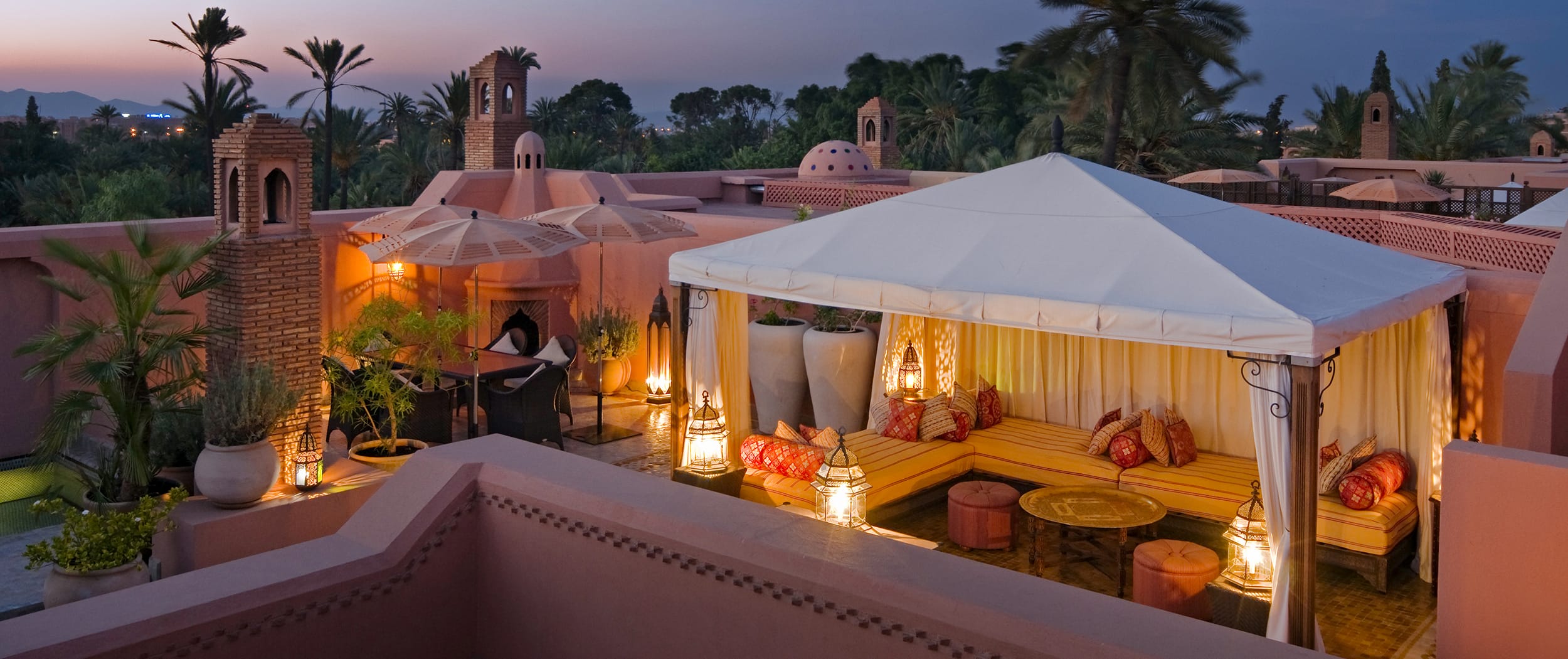 Rooftop terrace with seating area, decorative lanterns, and canopy, set against a tropical evening sky.