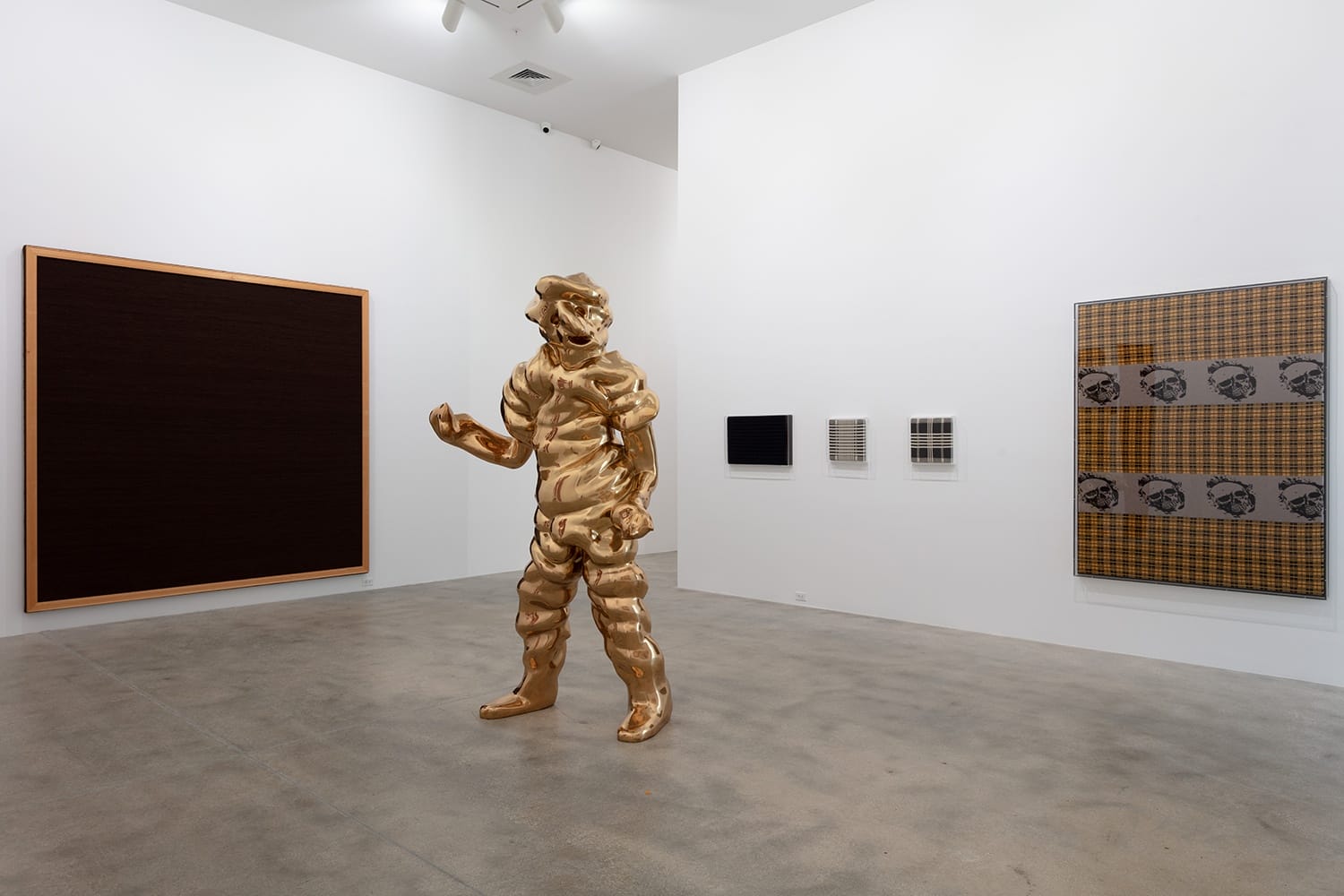 Art gallery installation featuring a shiny abstract sculpture, a large dark canvas, and various patterned artworks on white walls.