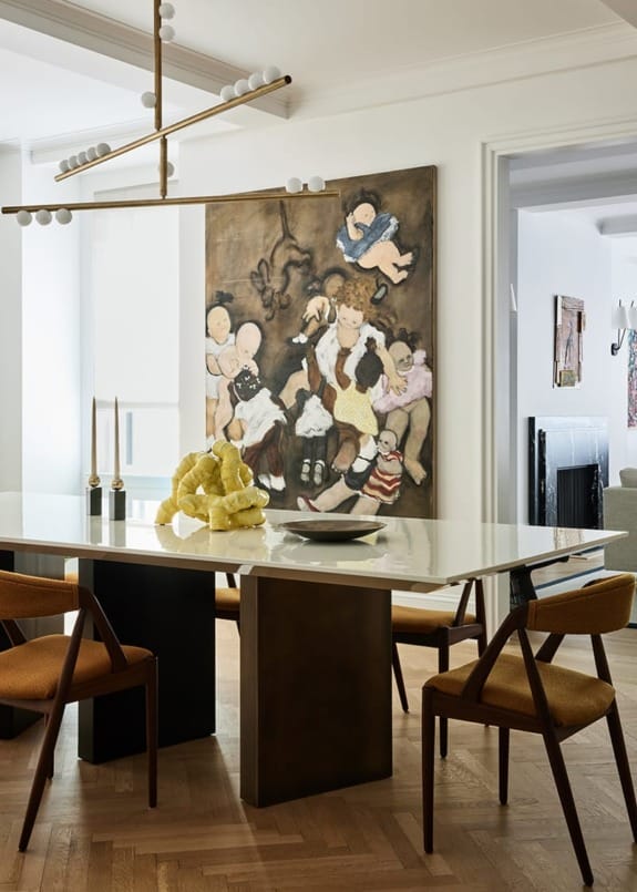 Modern dining room with a white table, contemporary chairs, abstract chandelier, and a large painting of children on the wall.