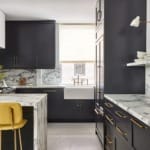 Modern kitchen with dark cabinets, marble countertops, and yellow bar stools, featuring a farmhouse sink and bright window.