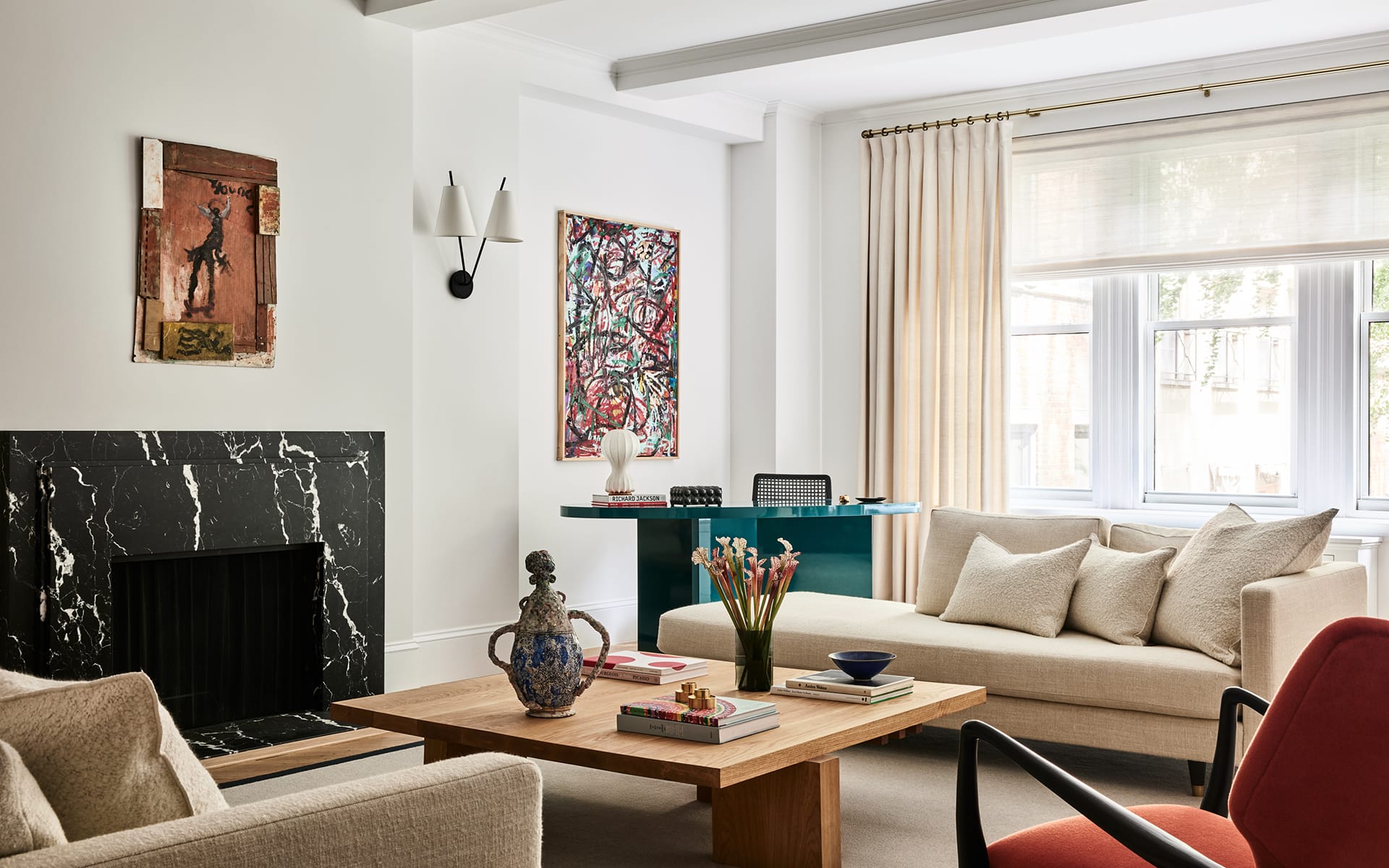 modern living room with beige sofas, wooden coffee table, colorful artwork, black fireplace, and large windows with curtains