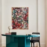 Modern interior with a teal desk, abstract art on the wall, and a black chair in a stylish, minimalistic setting.