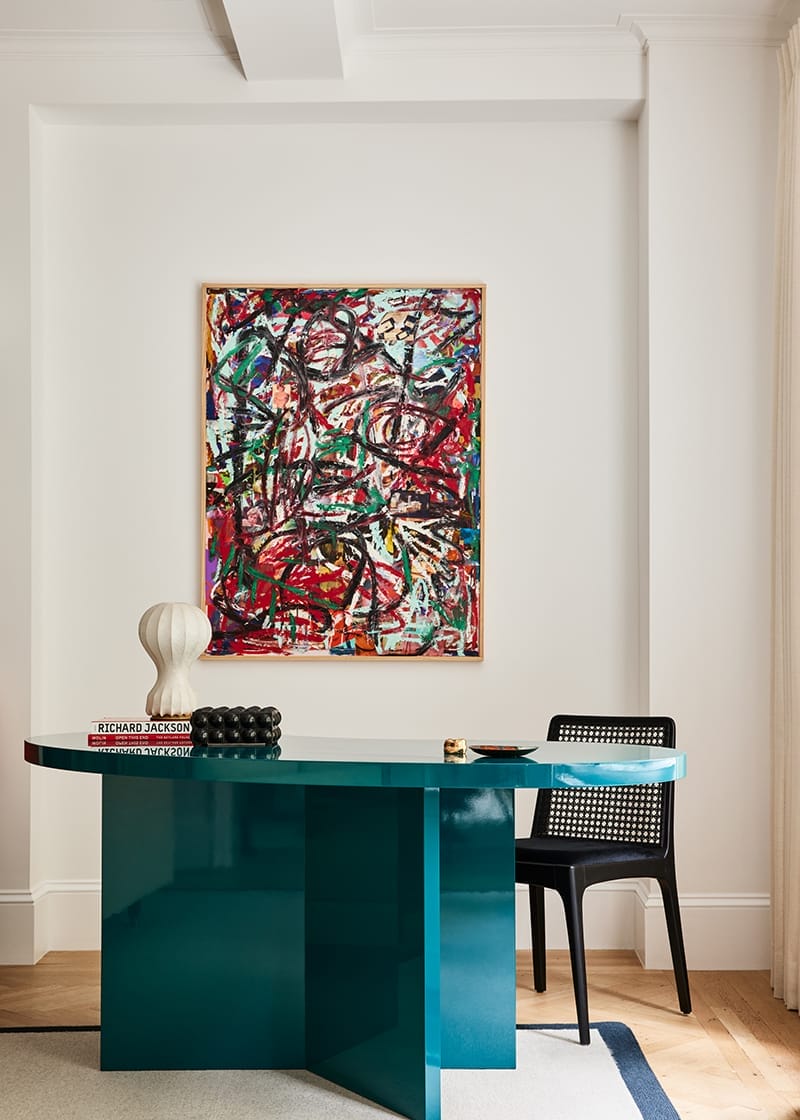 Modern interior with a teal desk, abstract art on the wall, and a black chair in a stylish, minimalistic setting.