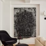 Modern living room with abstract black and white art on the wall, featuring a dark chair, small table, and a light-colored sofa.