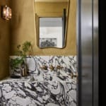 Modern bathroom with marble sink, gold accents, ornate mirror, and decorative vase with green plant.
