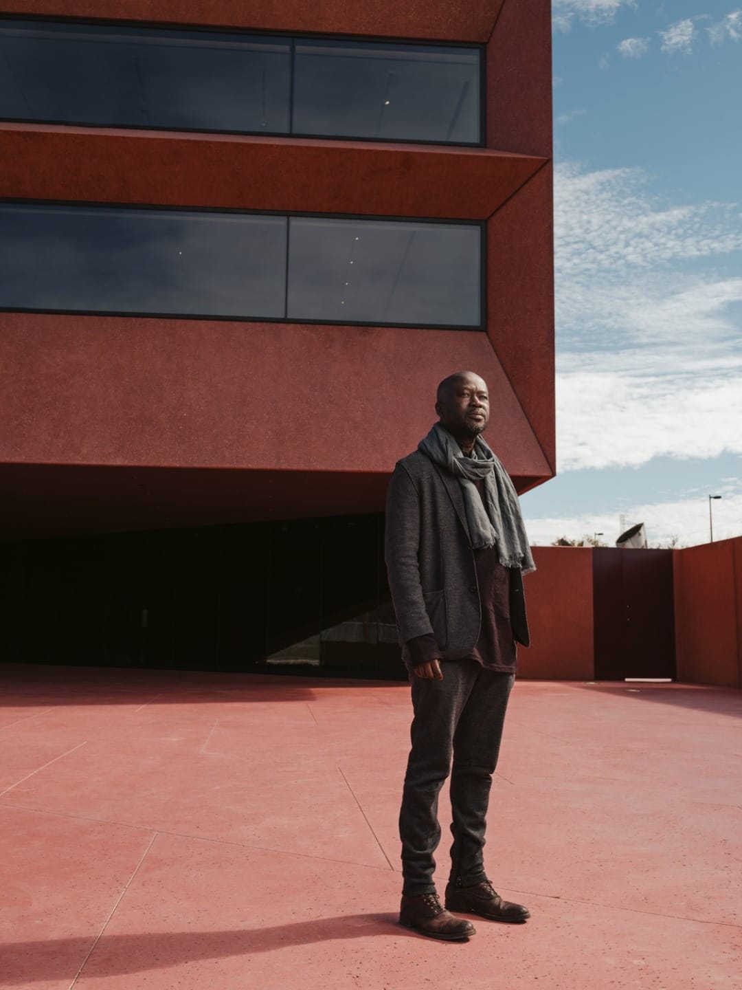 Person standing on a red concrete surface in front of a modern building under a partly cloudy sky.