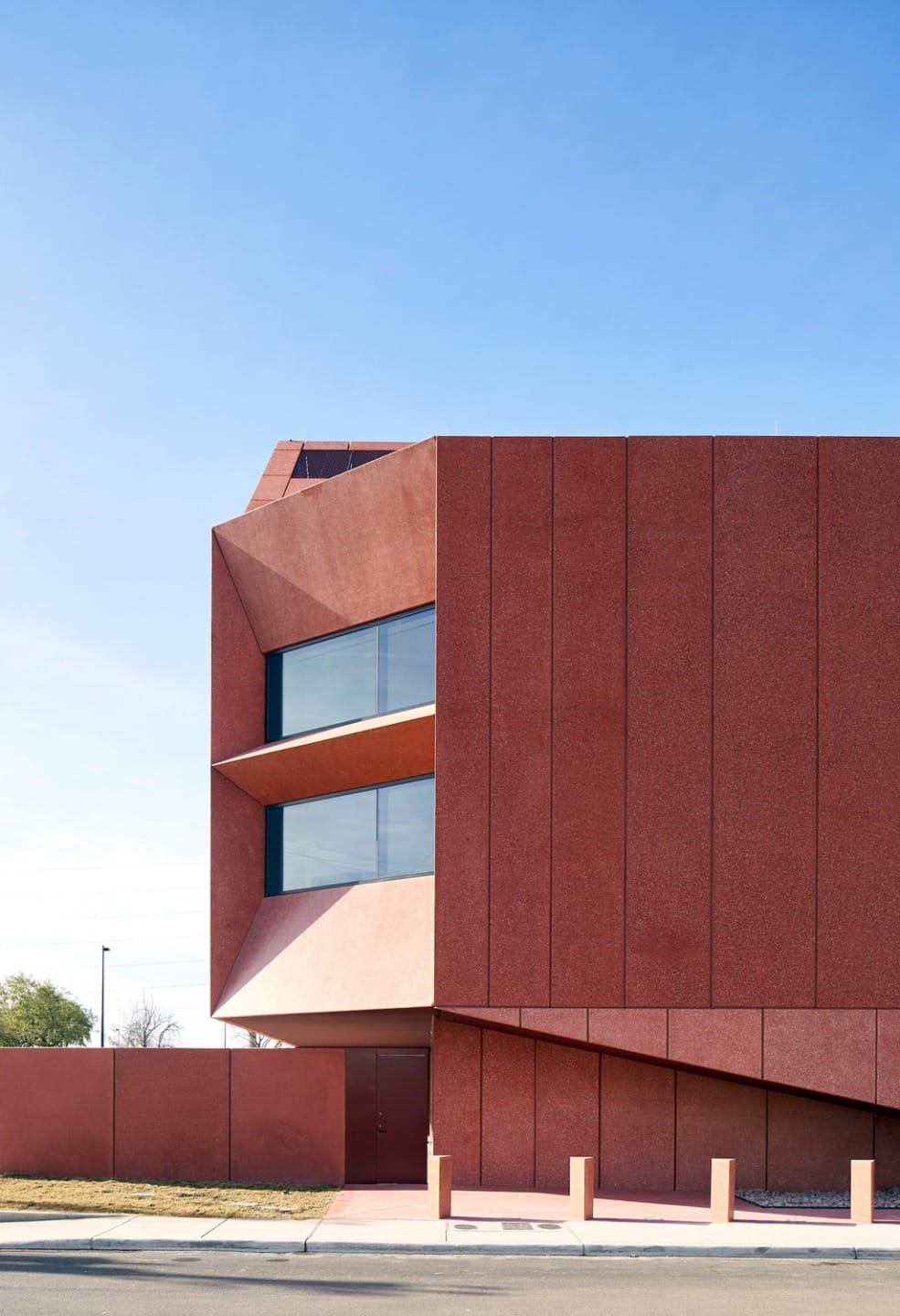 Modern building with angular red facade and large windows against a clear blue sky.