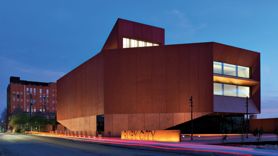 Modern architectural building with illuminated windows at dusk, featuring a distinctive angular design and warm-toned exterior.