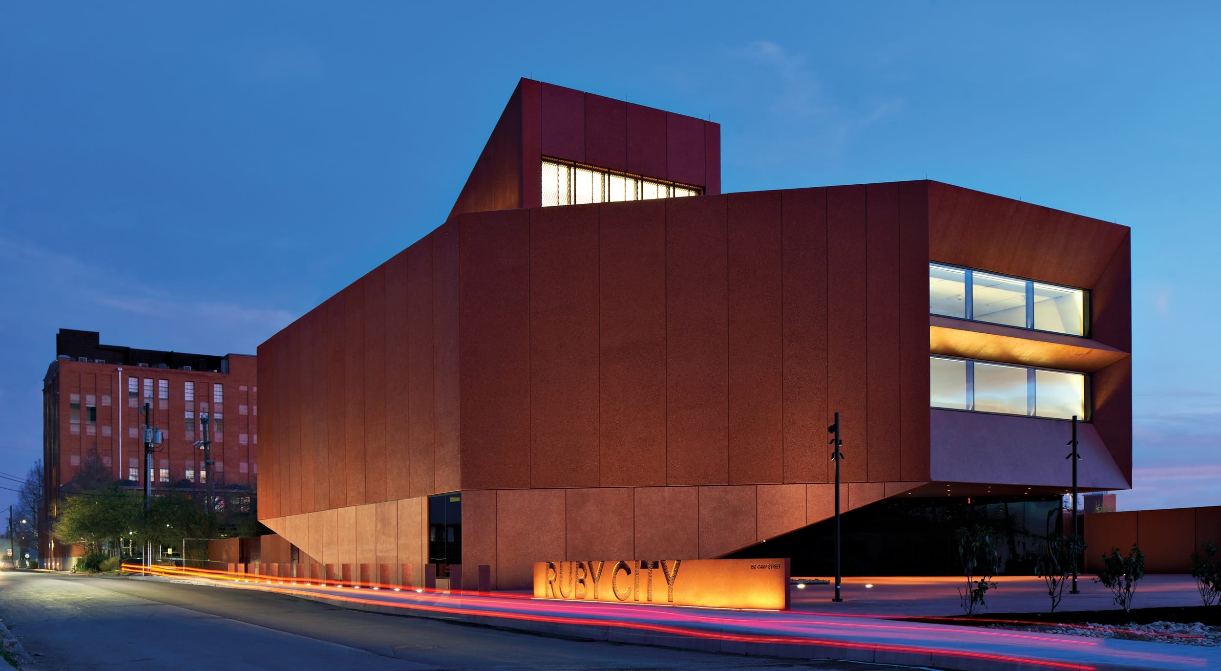 Modern architectural building with illuminated windows at dusk, featuring a distinctive angular design and warm-toned exterior.