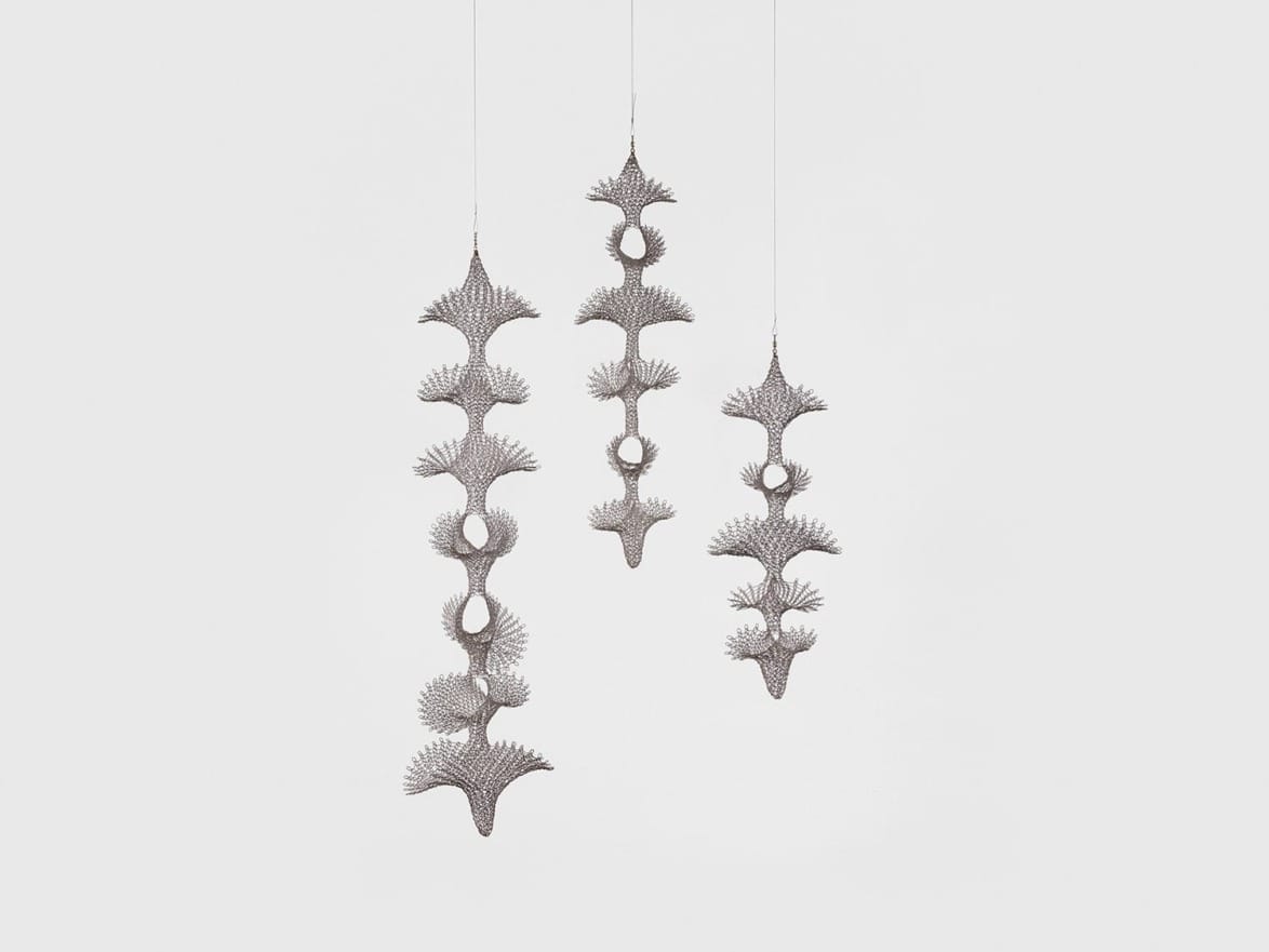 Three intricate, vertically hanging metallic sculptures with organic, branching designs against a light background.
