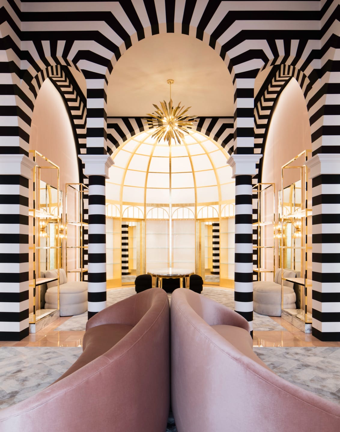 Luxurious lobby with black and white striped arches, pink curved sofas, and a golden starburst chandelier.