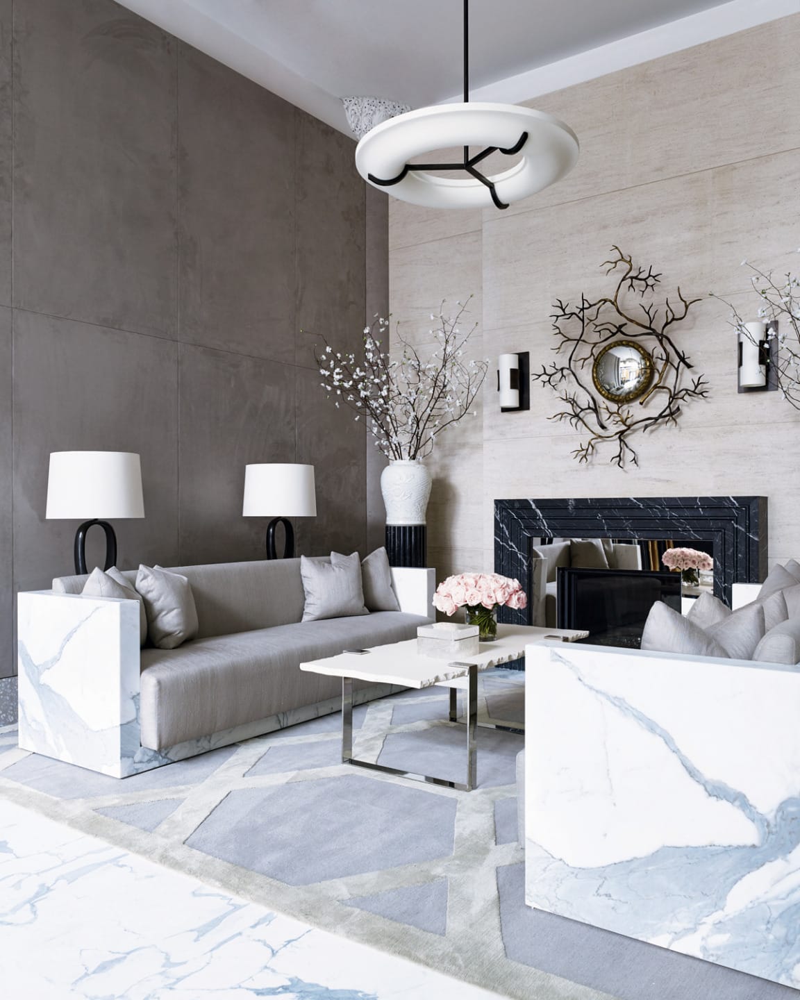 Modern living room with a gray sofa, marble accents, decorative mirror, and contemporary chandelier.