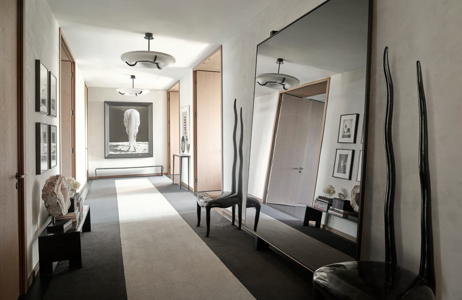 Modern hallway with large mirror, abstract art, and stylish decor featuring unique chairs and neutral tones.