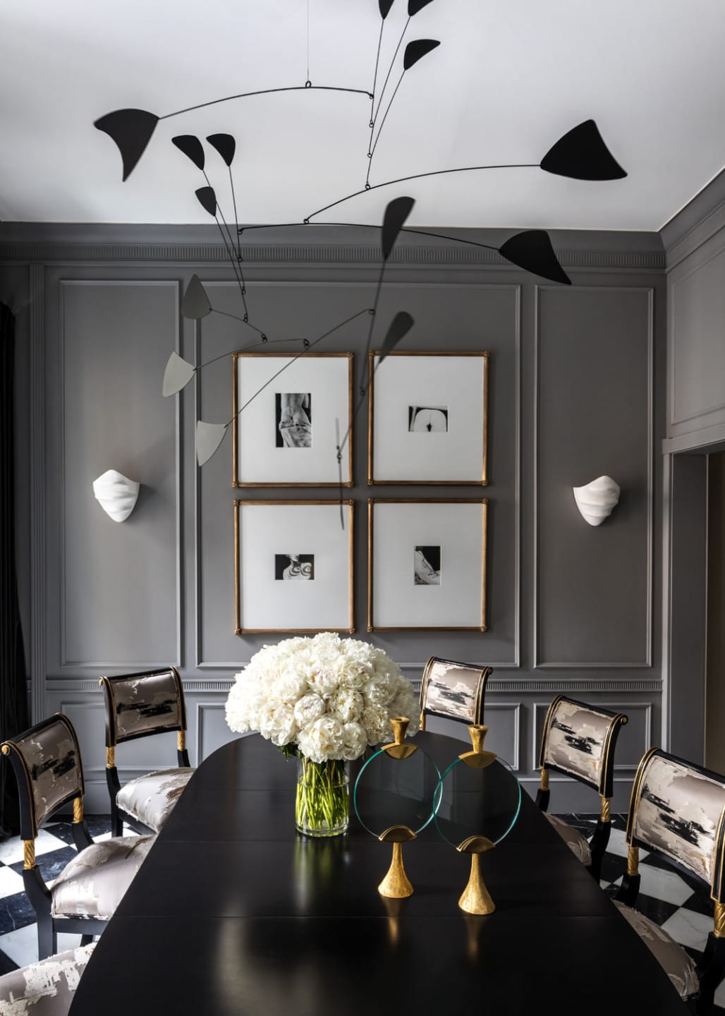 Elegant dining room with modern art mobile, black chairs, and a black table with white flowers in a vase.