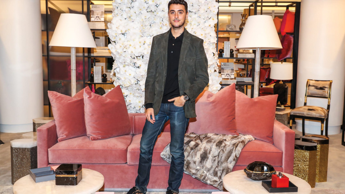 Person standing in a stylish living room with pink sofa, white floral wall, and elegant decor.