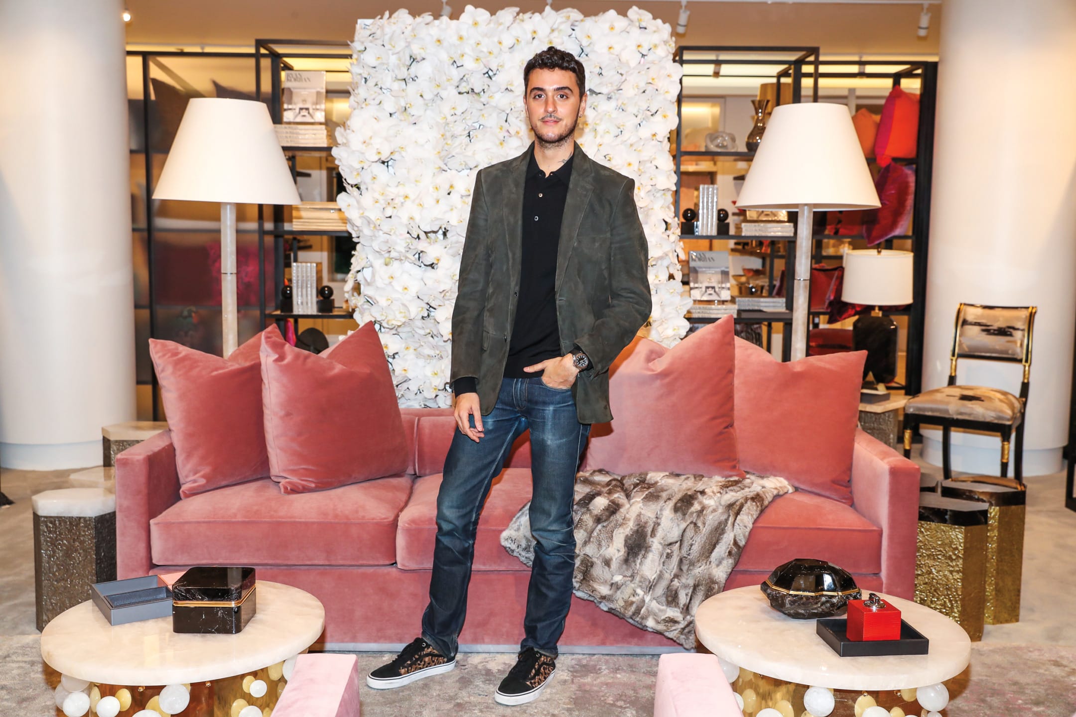Person standing in a stylish living room with pink sofa, white floral wall, and elegant decor.