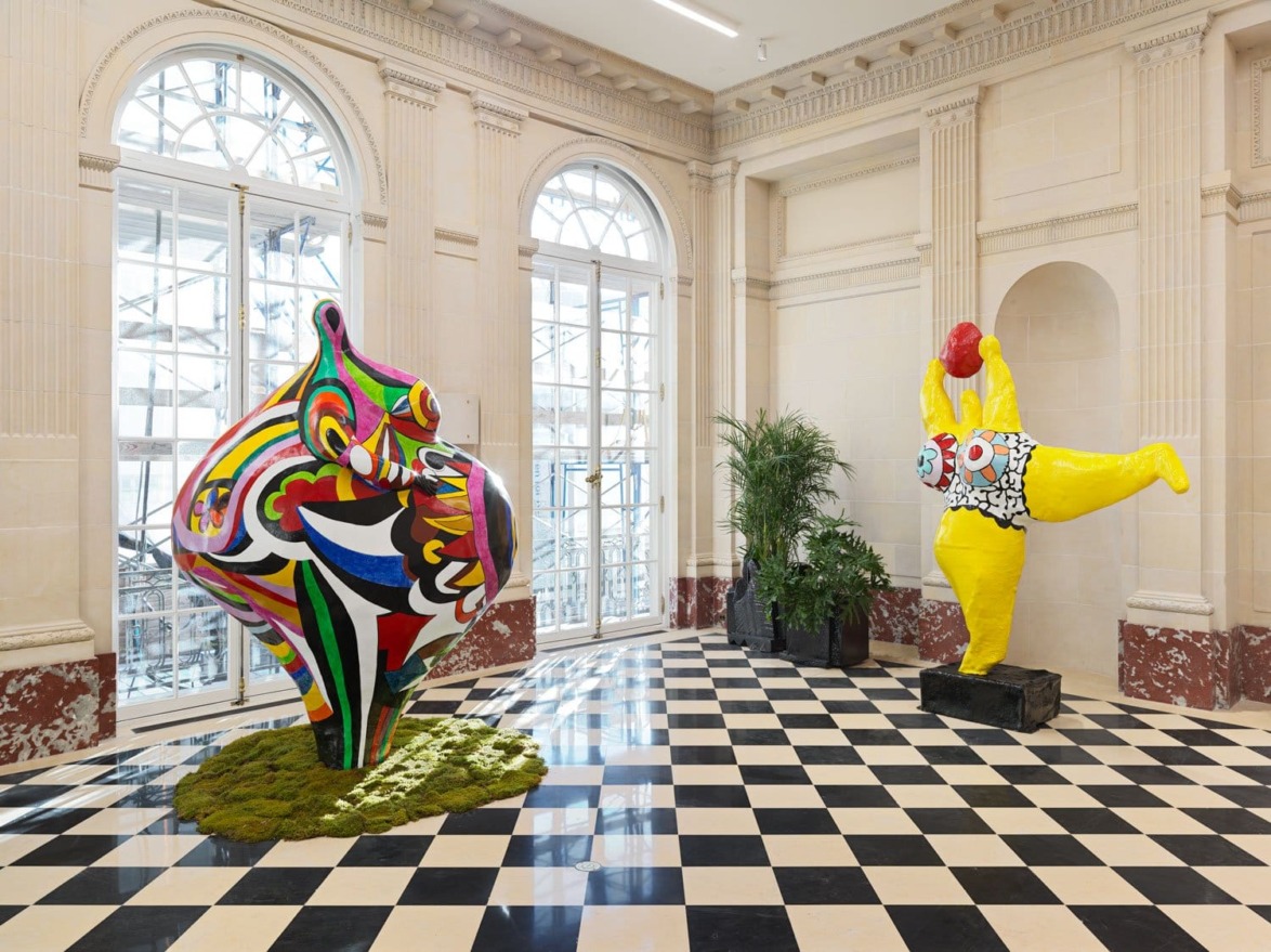 Colorful abstract sculptures displayed in an art gallery with checkered floor and large windows.