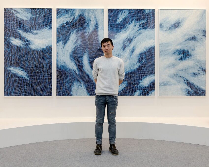 Person standing in front of a series of four abstract blue and white paintings in a gallery setting.