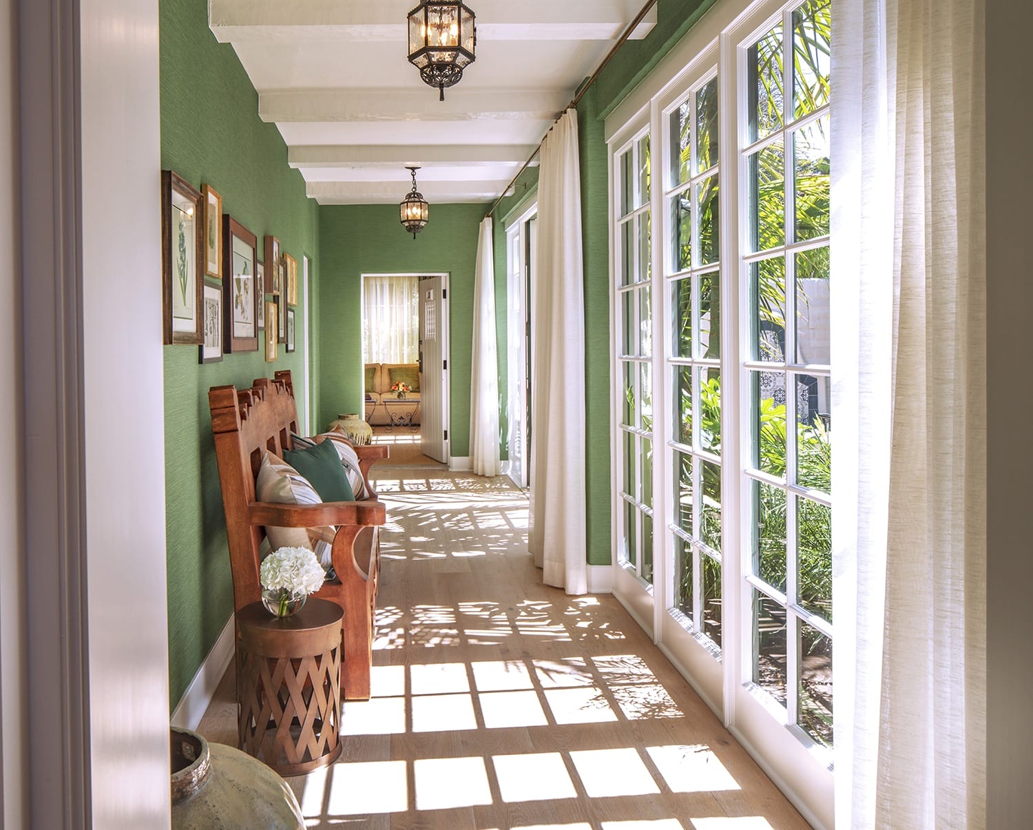 Bright sunroom with green walls, large windows, wooden chairs, and potted plants, creating a cozy and inviting atmosphere.